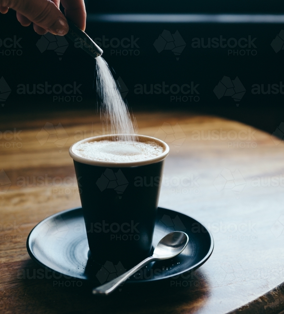 Action of pouring a sachet of sugar into a cafe latte at a restaurant - Australian Stock Image