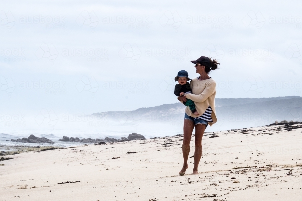 Active Mother carrying baby boy along remote coastline - Australian Stock Image