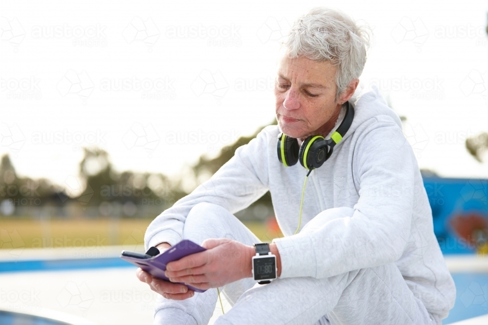 Active senior lady checking phone listening to music with headphones - Australian Stock Image