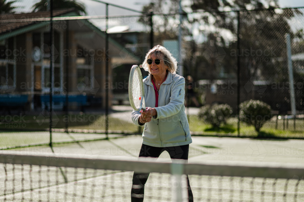 Active senior woman enjoys playing tennis at a local court. - Australian Stock Image