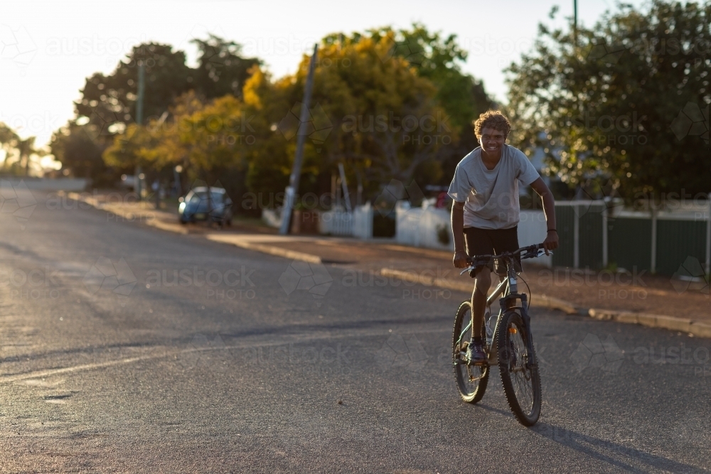 adolescent boy riding bicycle on quiet street with no helmet - Australian Stock Image