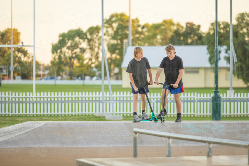 Adolescent teenage boys hanging out at the skate park with scooters - Australian Stock Image