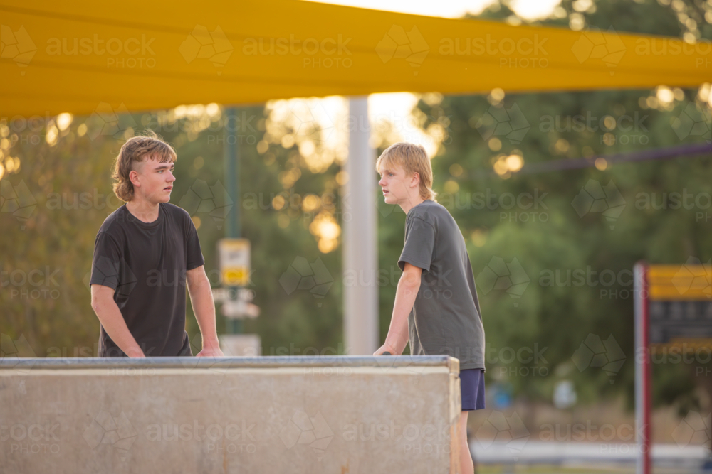 Adolescent teenage boys hanging out at the skate park with scooters - Australian Stock Image