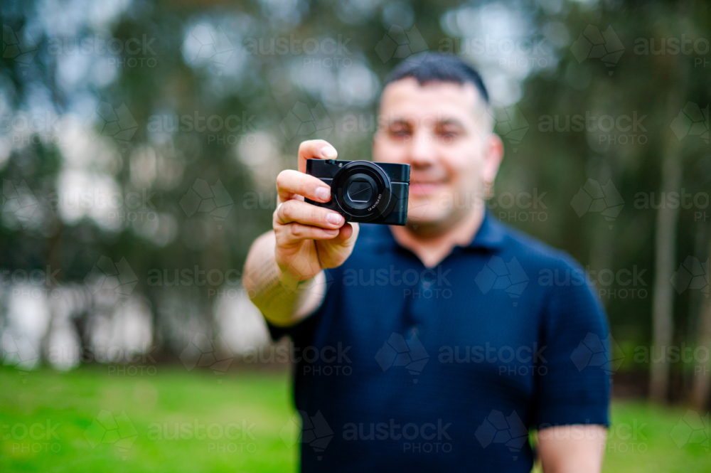 Adult male holding a camera in a park, enjoying a day outdoors while capturing moments - Australian Stock Image