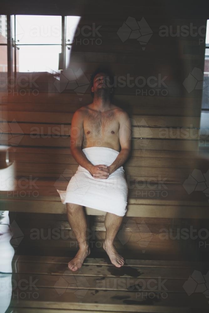 Adult male through window sitting in sauna with pool reflection - Australian Stock Image