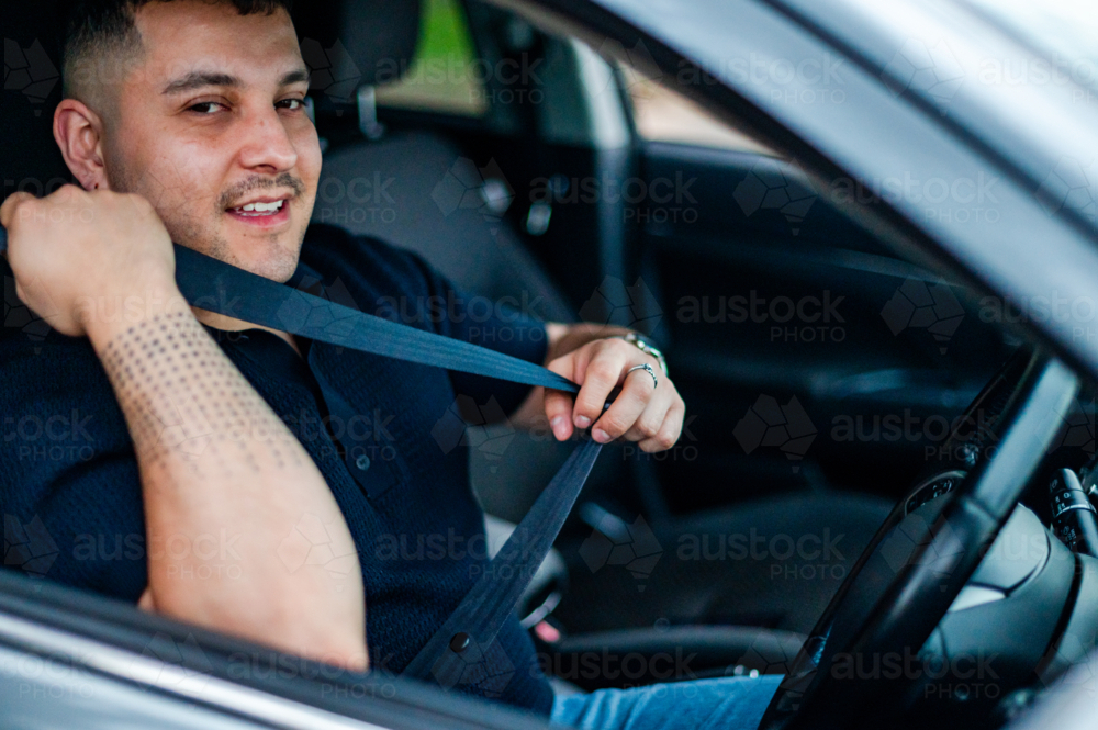 Adult man adjusts his seatbelt while parked in a park, ready for adventure - Australian Stock Image