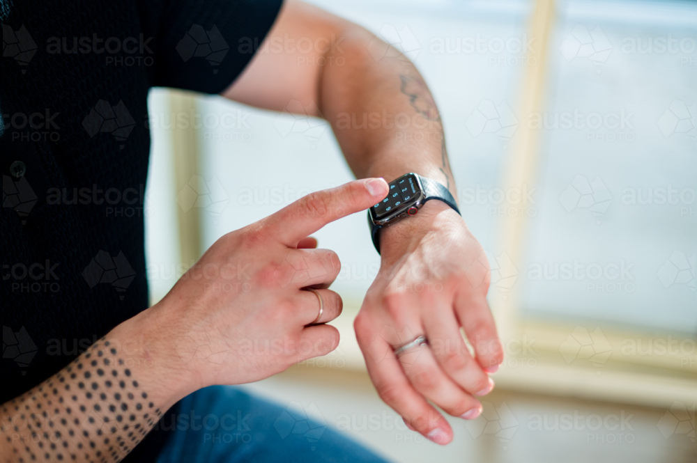 Adult man uses his smart watch to check notifications while seated indoors - Australian Stock Image