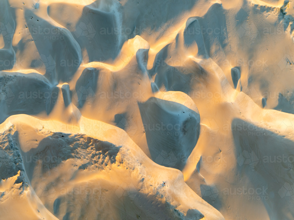 Aerial close-up of sculpted sand dunes with golden light and shadow creating abstract patterns - Australian Stock Image