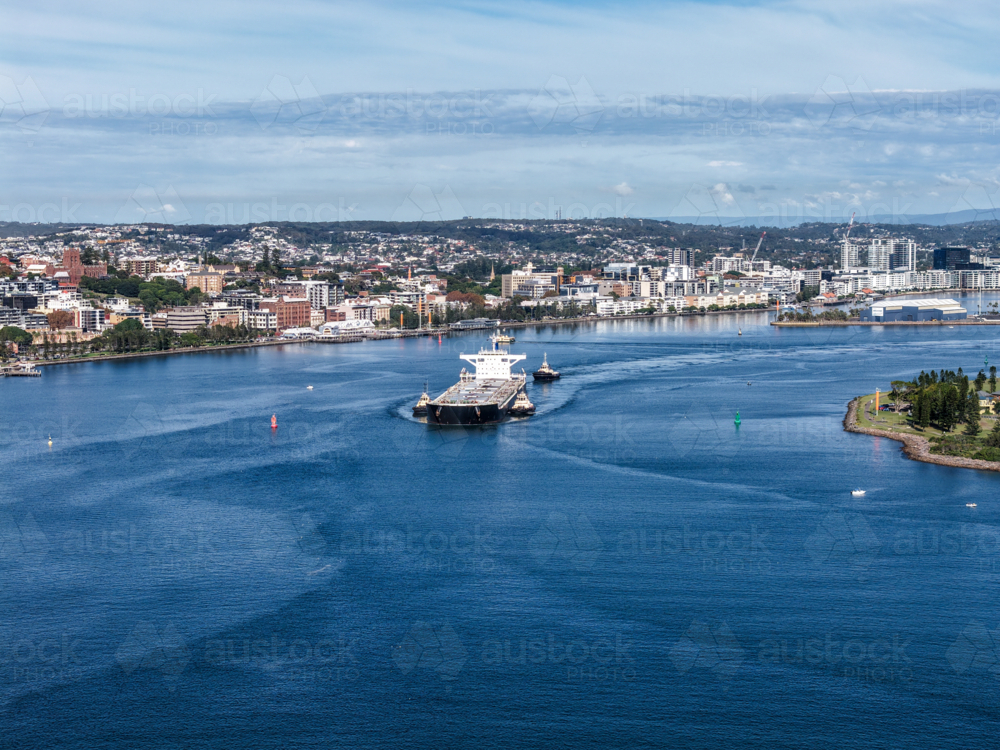 Aerial drone view of a large cargo ship being escorted by tug boats through Newcastle Harbour. - Australian Stock Image