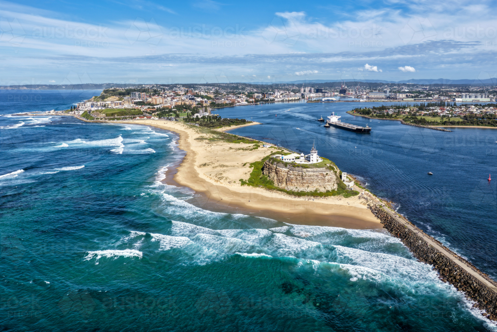 Aerial drone view of Nobbys Lighthouse and Nobbys Beach with a large cargo ship being escorted. - Australian Stock Image