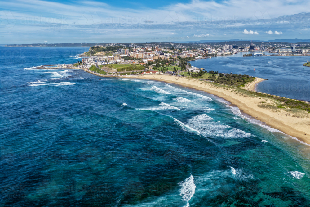 Aerial drone view of waves rolling onto the sandy shoreline at Nobbys Beach with Newcastle city - Australian Stock Image