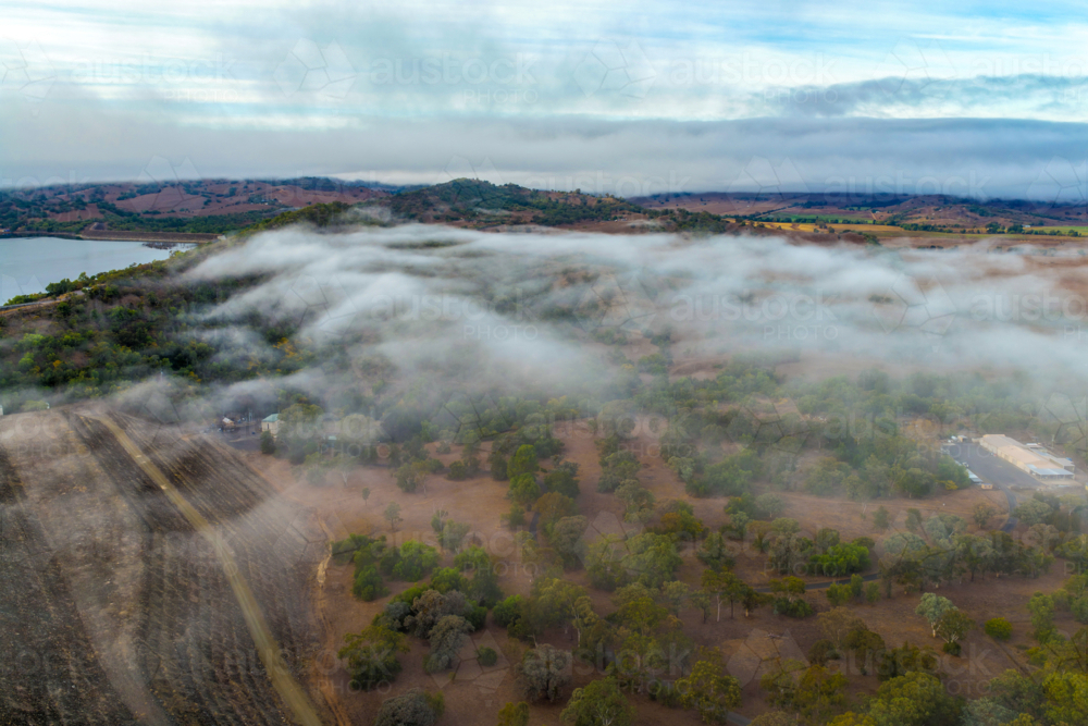 Aerial image of the Glenbawn Dam wall with morning fog drifting through the surrounding valley - Australian Stock Image