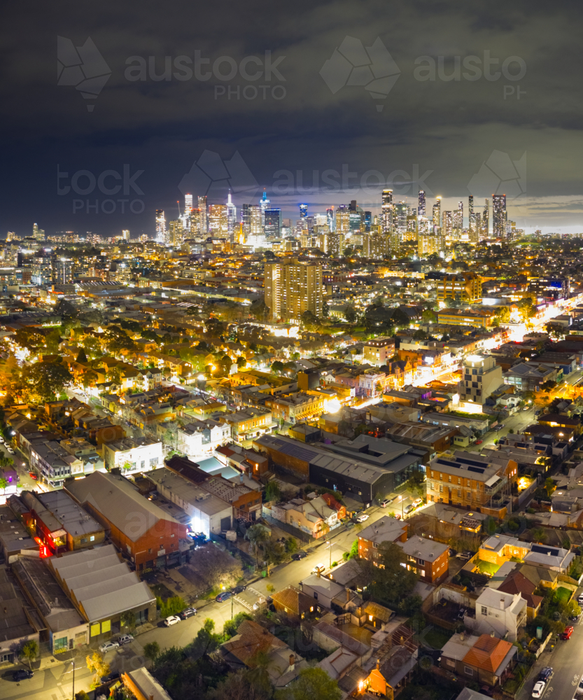 Aerial night time view of colourful city lights over an urban streetscape and distant city skyline - Australian Stock Image