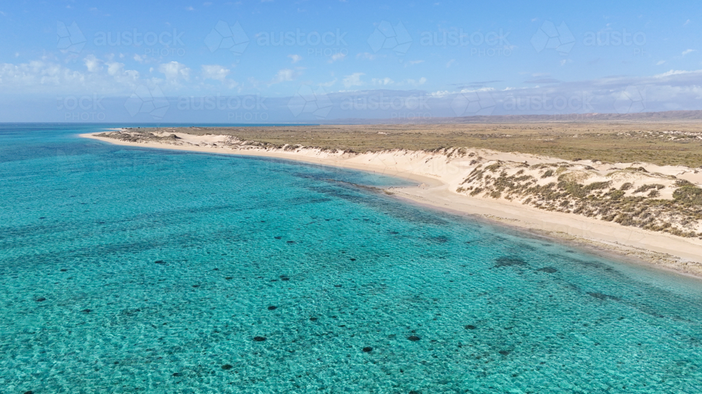 Aerial of a remote beach with turquoise water surrounded by sand dunes - Australian Stock Image
