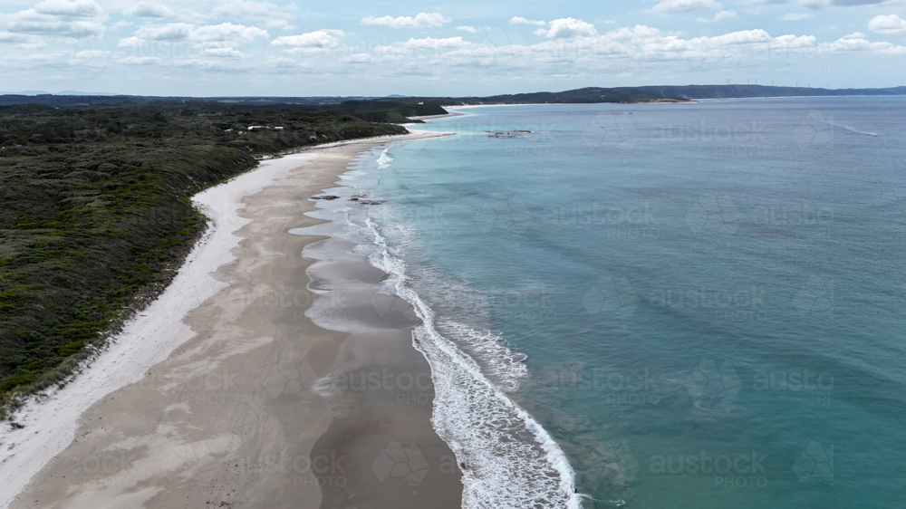 Aerial of an empty beach on a cloudy day with a retreating tide - Australian Stock Image