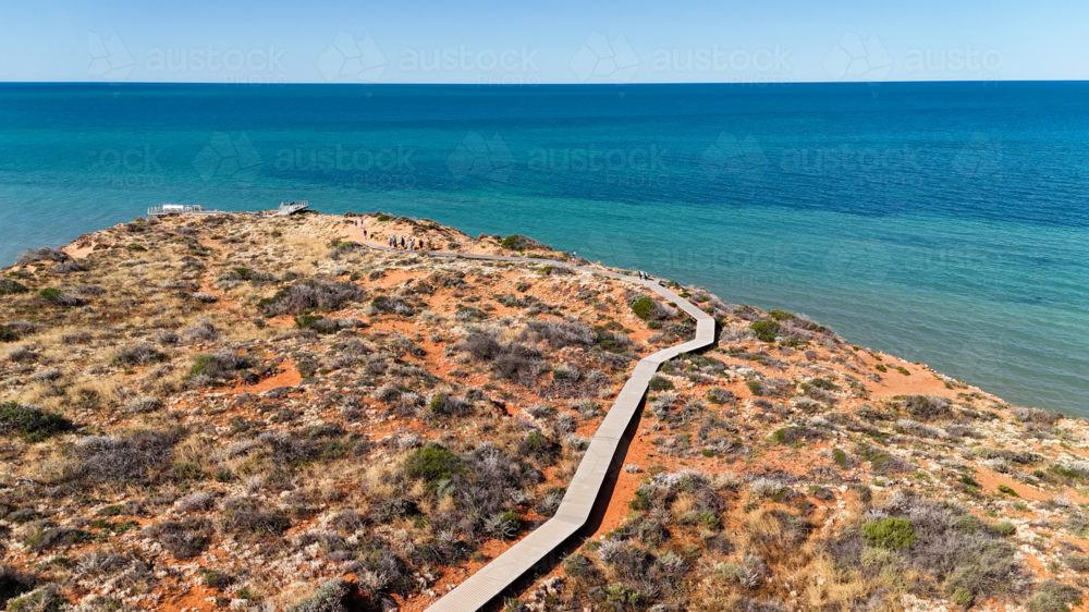 Aerial of boardwalk out to a point on a red sand cliff by the water - Australian Stock Image