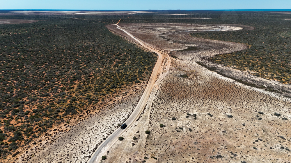 Aerial of car driving on a road through a clay pan - Australian Stock Image