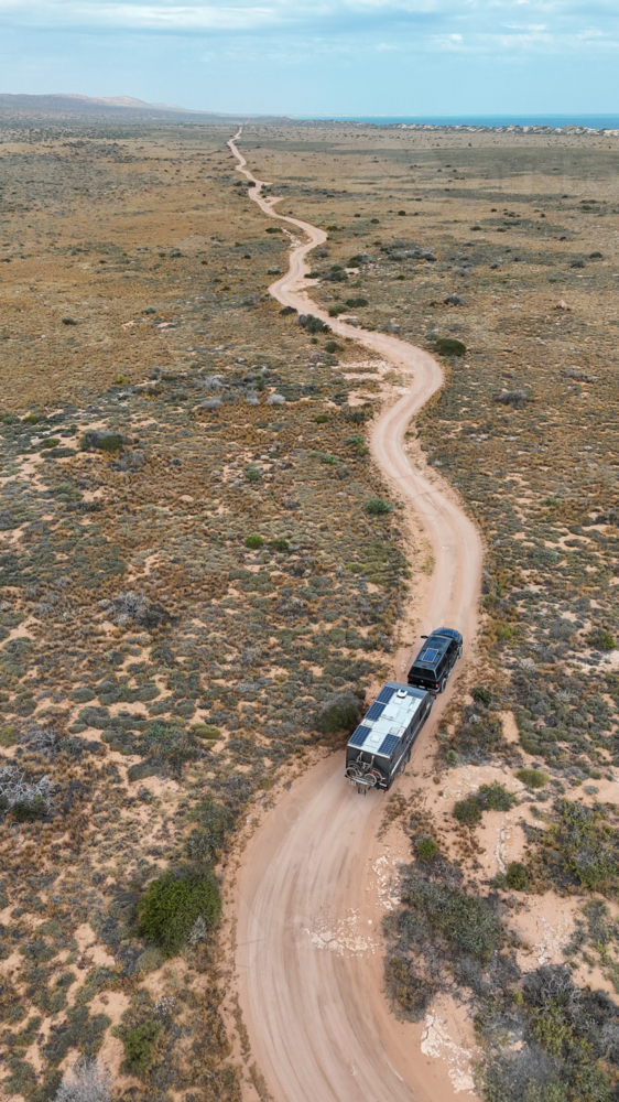 Aerial of caravan driving along bending dirt road - Australian Stock Image