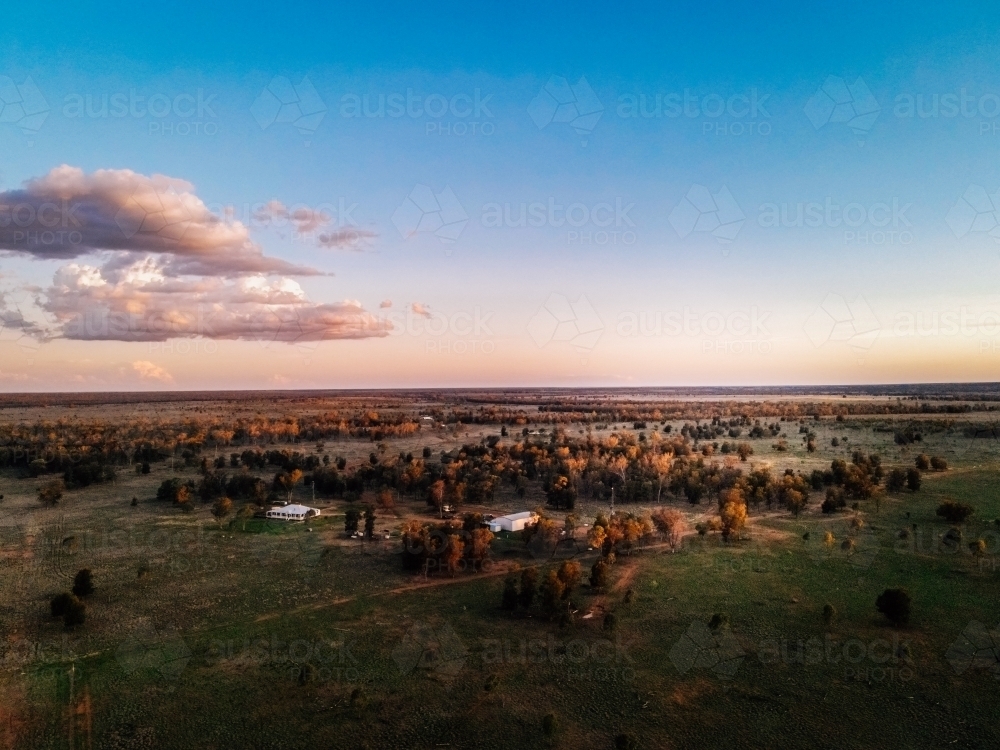 Aerial of flat land, trees, 2 small sheds with blue sky and clouds - Australian Stock Image