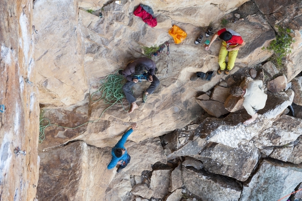 Aerial of four male rock climbers at the bottom of a crag - Australian Stock Image