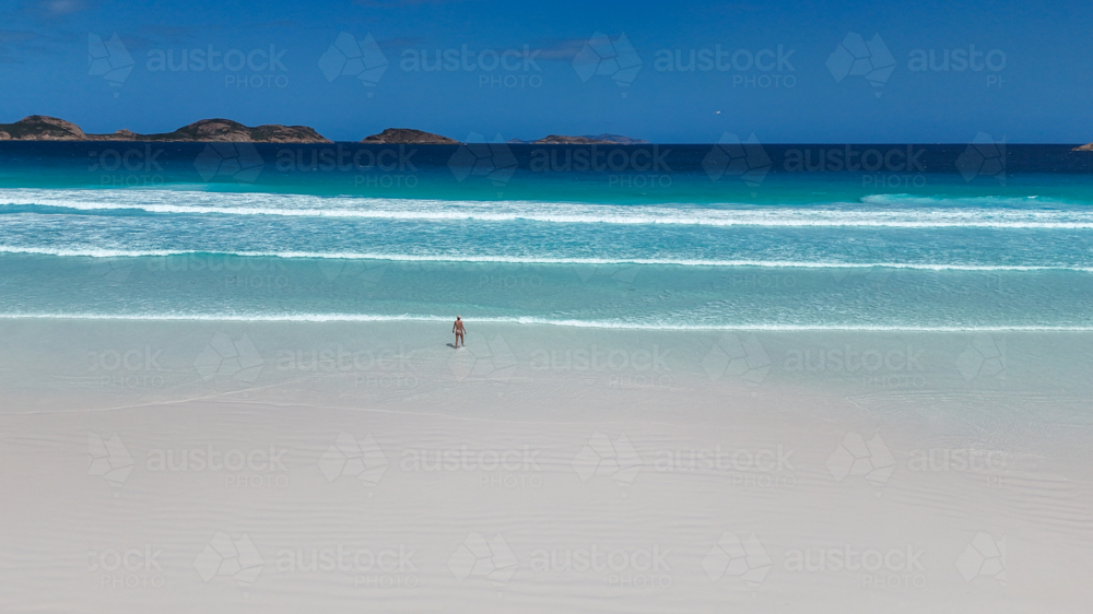 Aerial of girl walking into water at beach with white sand and crystal blue water - Australian Stock Image