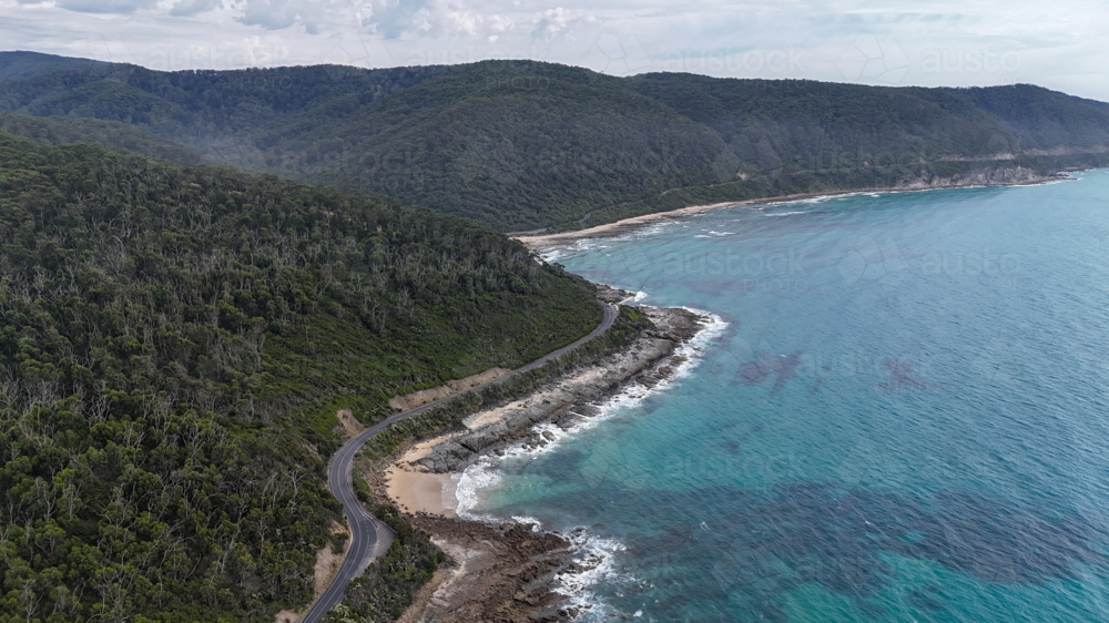 Aerial of road bending along mountains by the ocean - Australian Stock Image