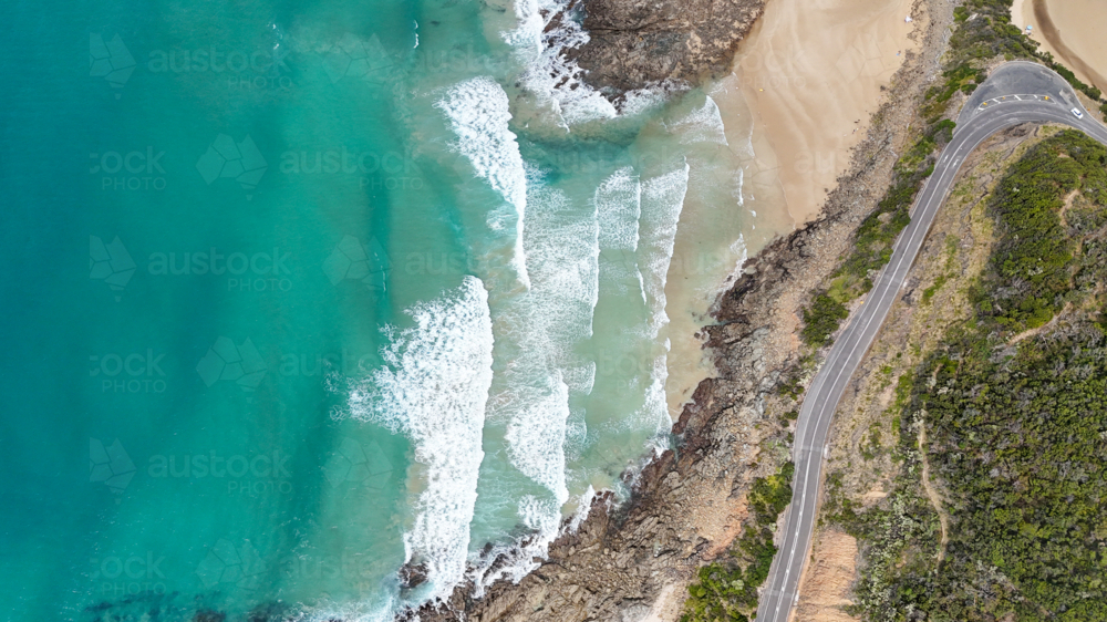 Aerial of road bending around beach with waves - Australian Stock Image