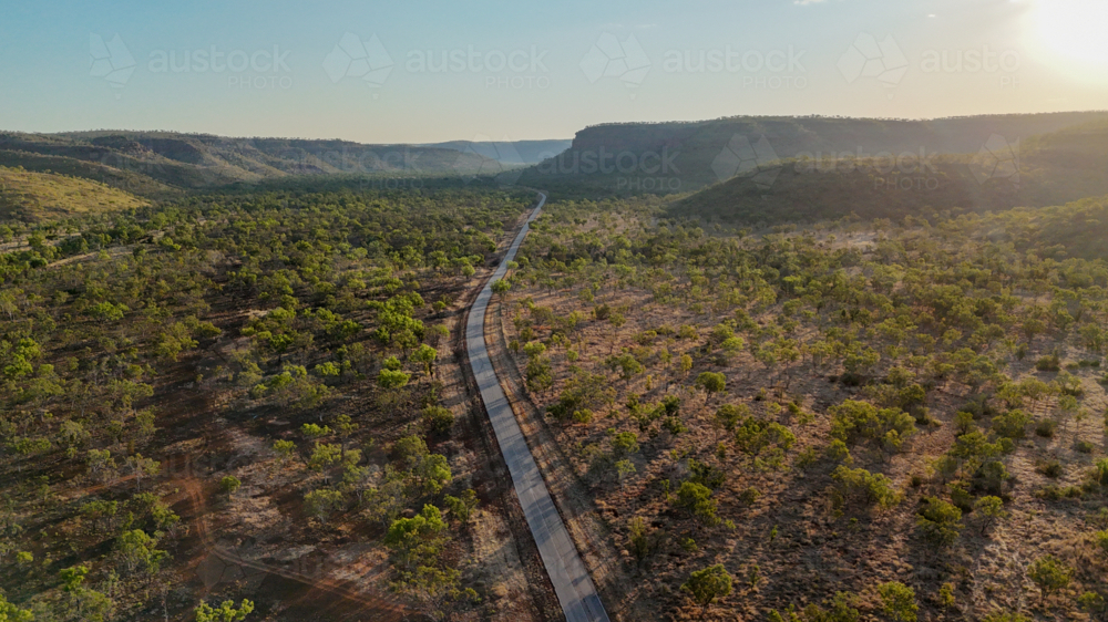 Aerial of road through forest landscape at golden hour - Australian Stock Image