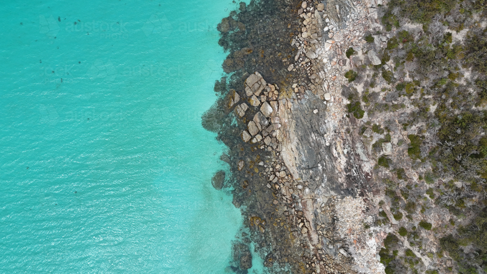Aerial of rocky edge meeting bright aqua water - Australian Stock Image