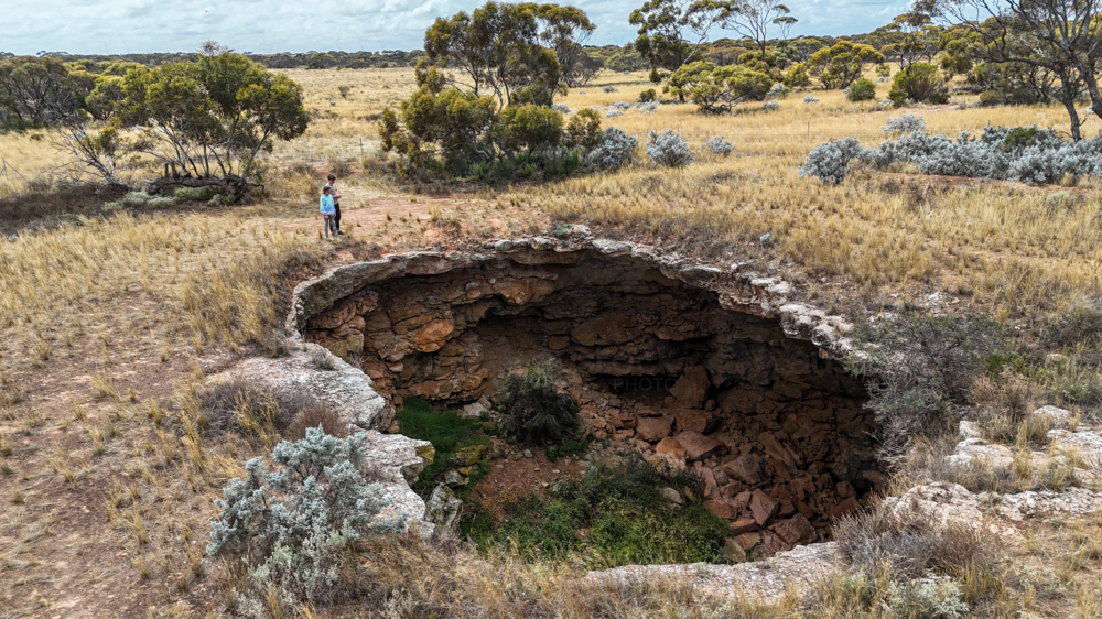 Aerial of two kids looking into a remote sinkhole - Australian Stock Image