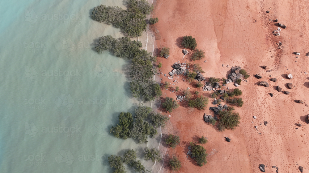 Aerial of water meeting red sand with bushes and rocks - Australian Stock Image