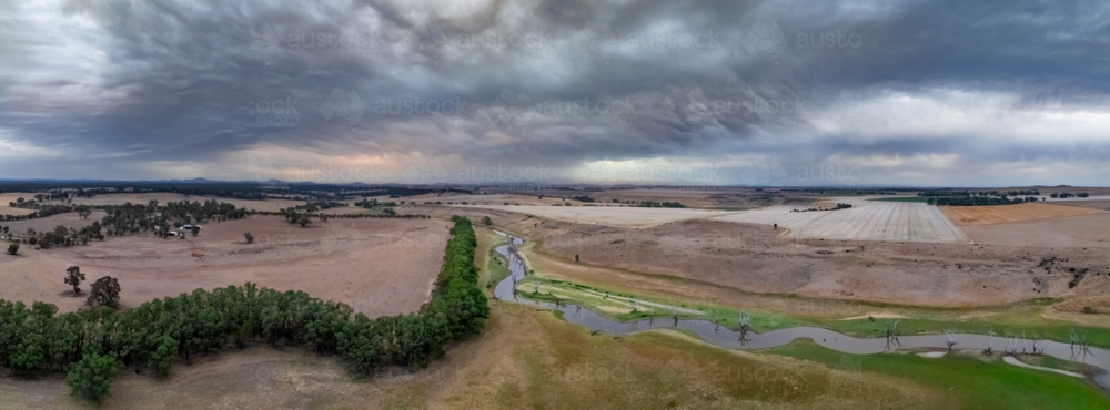 Aerial panorama of a dark sunset sky over a meandering river through dry farmland - Australian Stock Image