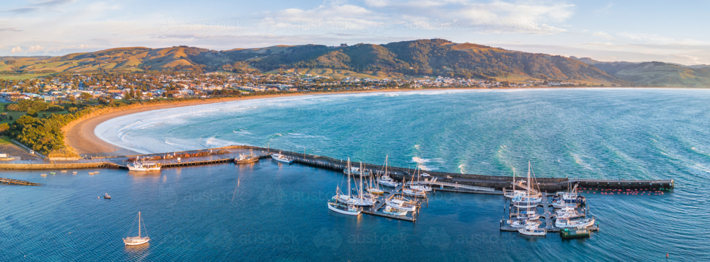 Aerial panorama of boats in a coastal harbour in front of a seaside town and hills - Australian Stock Image
