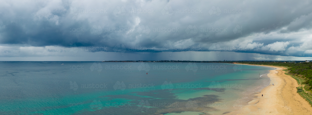 Aerial panorama of rain falling from a wide stormfront advancing over a calm bay and sandy beach - Australian Stock Image