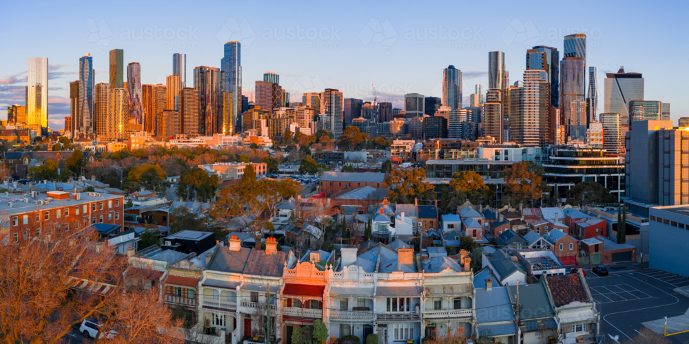 Aerial panorama of terrace houses in a suburban street in front of a city skyline in golden light - Australian Stock Image