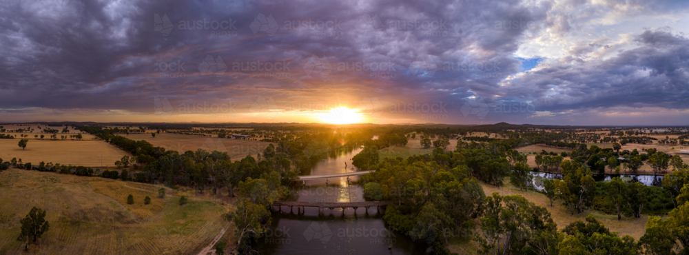 Aerial panorama view of colourful dramatic sunset over farmland alongside an inland river and bridge - Australian Stock Image