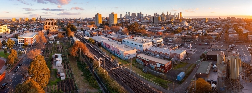 Aerial panoramic view of a busy city suburb at sunset with a railway line running through it - Australian Stock Image