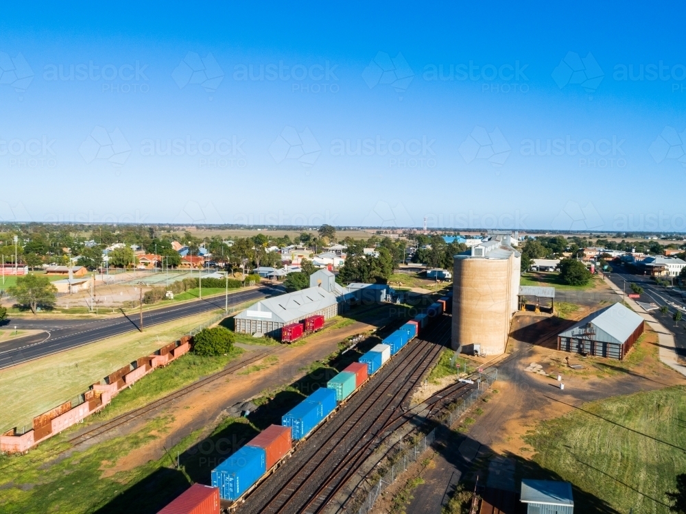 Aerial photo on sunlit day in country town of silos beside railway track and freight train - Australian Stock Image