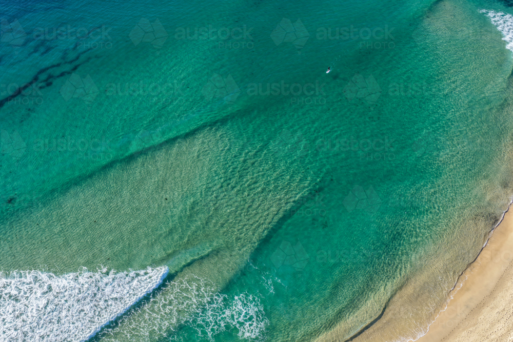 Aerial scene capturing a lone paddleboard rider in the clear turquoise waters at One Mile Beach. - Australian Stock Image