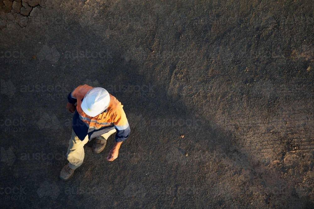Aerial shot a male person with a helmet and orange jacket on a black colored ground - Australian Stock Image