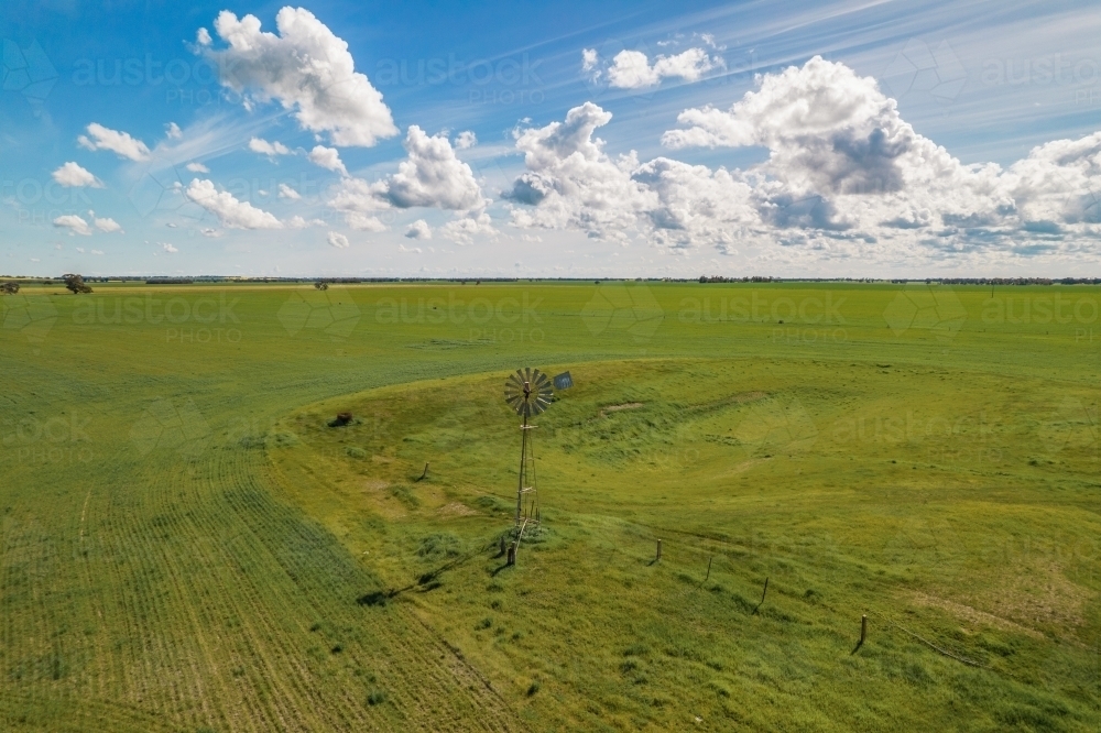 aerial shot of a big open field with a windmill under cloudy blue skies - Australian Stock Image