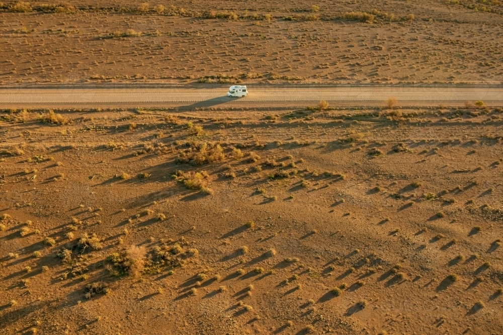 Aerial shot of campervan travelling alone along dirt road in outback - Australian Stock Image