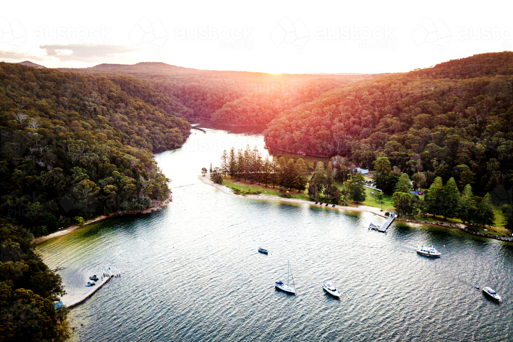 Aerial sunset over sheltered bay with boats and forested shoreline - Australian Stock Image