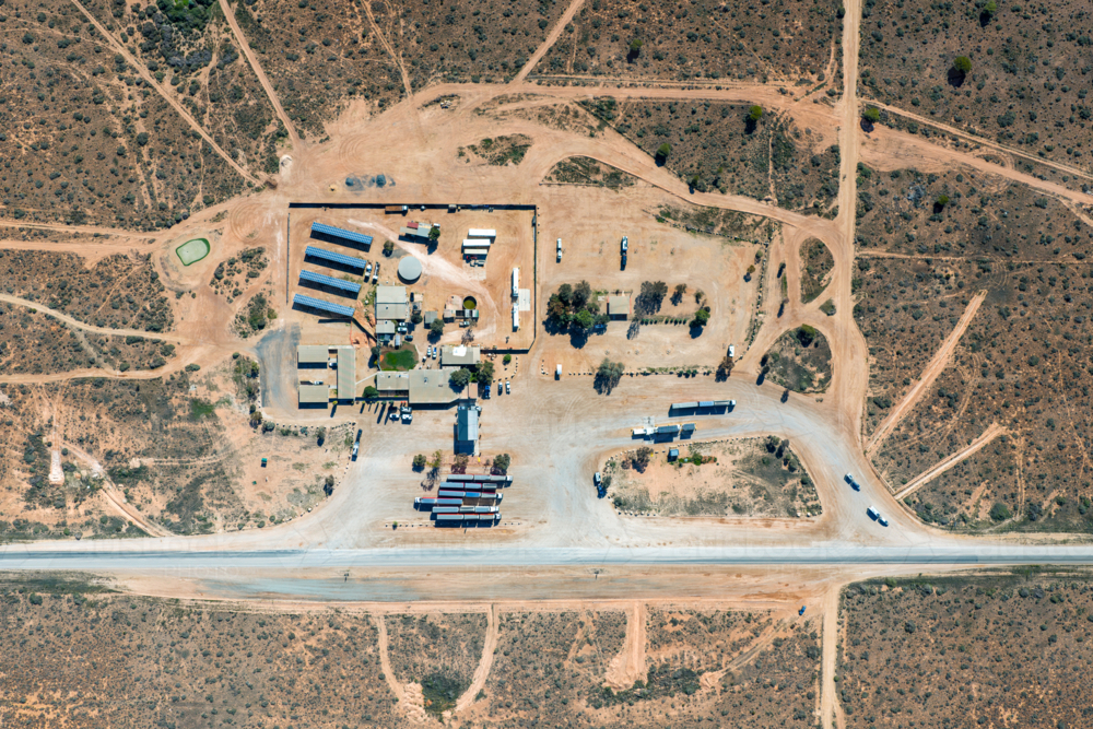 Aerial top-down view of a remote roadhouse with solar panels and trucks by a highway - Australian Stock Image