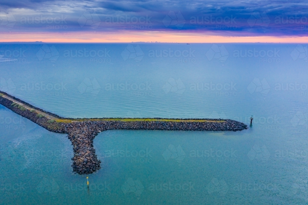 Aerial view a breakwater in a calm bay at sunset - Australian Stock Image