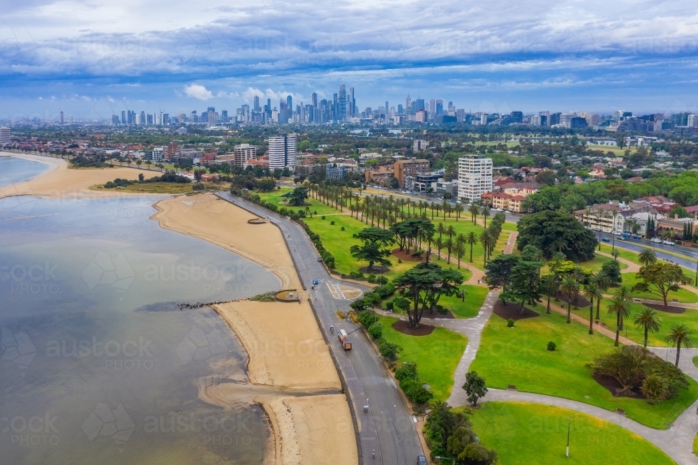 Aerial view a coast road, beach and parkland with a city in the background - Australian Stock Image