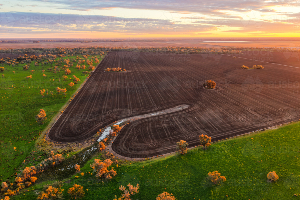 Aerial view capturing warm sunshine over cultivated fields surrounded by lush green countryside - Australian Stock Image