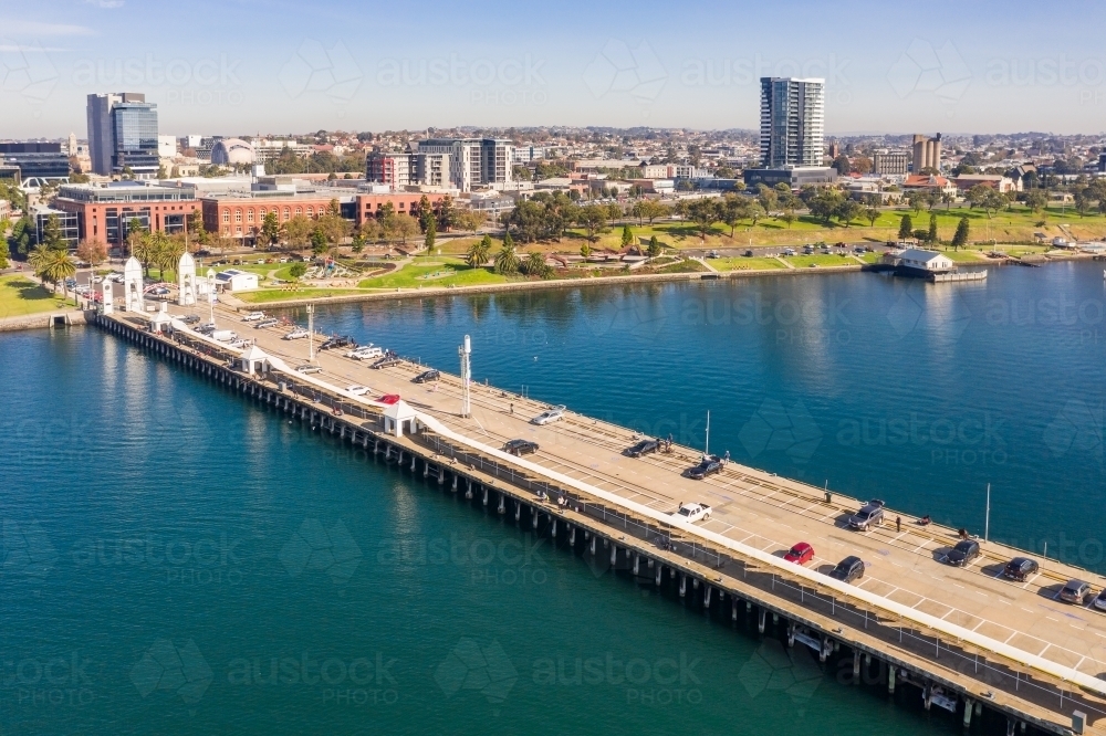 Aerial view looking along a coastal pier with car parking and a city in the background - Australian Stock Image