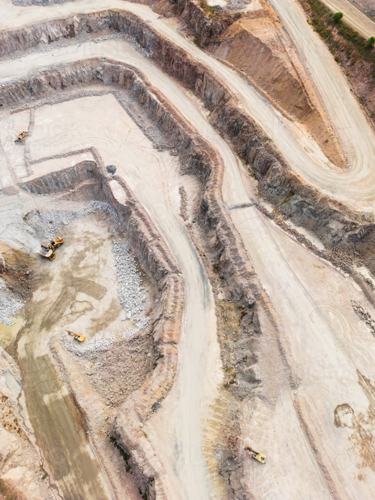 Aerial view looking down into a quarry pit with machinery on the ground - Australian Stock Image