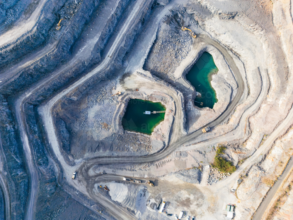Aerial view looking down into a tiered quarry pit with machinery and water ponds - Australian Stock Image